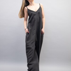 May include: A woman wearing a black sleeveless jumpsuit with a V-neckline. The jumpsuit has a relaxed fit and wide legs.