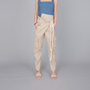 May include: A denim blue top with wide straps and a square neckline paired with beige cargo pants. The pants feature large pockets and a wrap-around waist with a white rope tie. The model is wearing light pink sandals.