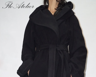 May include: A black coat with a large hood, long sleeves, and a matching tie belt at the waist. The coat features a wide lapel design and reaches below the knees. The text Flo Atelier is visible in the upper left corner of the image.
