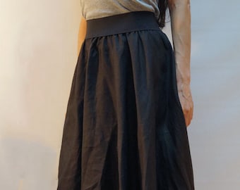 May include: A black maxi skirt with a wide waistband. The skirt is made of a soft, flowing fabric and has a simple, elegant design.