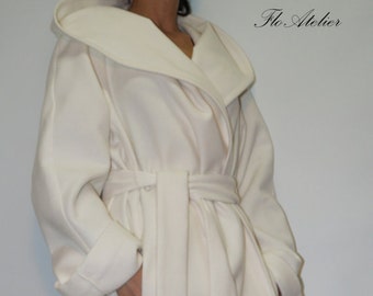May include: An off-white hooded coat featuring a wide shawl collar, long sleeves with cuffs, and a matching fabric tie belt at the waist. The garment has two side pockets and the text Flo Atelier is printed in the upper right corner of the image.