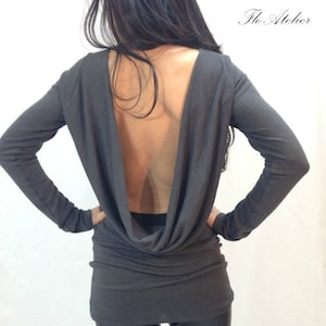 Peut inclure: Un chemisier à manches longues gris anthracite avec un col montant profond et un dos nu. Le chemisier est fait d'un tissu doux et extensible et a une coupe décontractée.