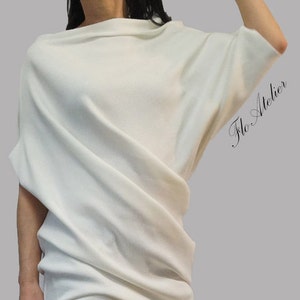 May include: A white, ribbed, off-the-shoulder top with a draped design. The top is paired with black, distressed jeans and black ankle boots.