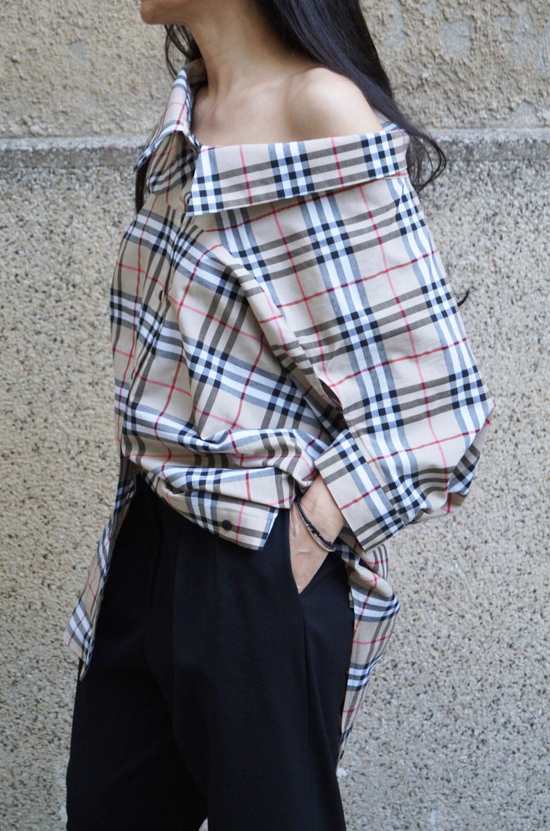 May include: A beige, black and red plaid off-the-shoulder shirt with long sleeves. The shirt is oversized and has a relaxed fit.