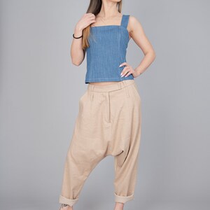 May include: A woman wearing a light blue denim tank top and beige linen trousers. She is wearing beige heeled sandals.