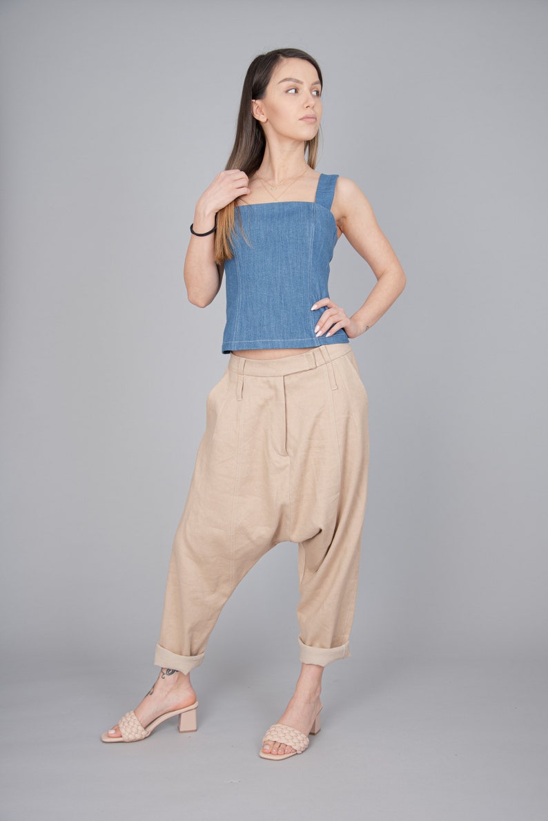 May include: A woman wearing a light blue denim tank top and beige linen trousers. She is wearing beige heeled sandals.