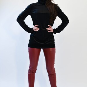 May include: A woman wearing a black turtleneck sweater and burgundy leather pants. She is wearing round sunglasses and black heeled boots.