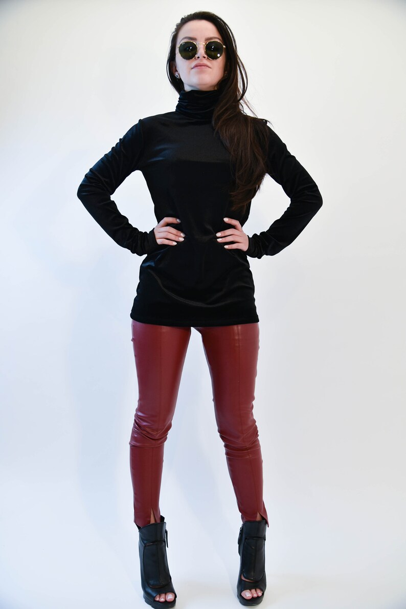 May include: A woman wearing a black turtleneck sweater and burgundy leather pants. She is wearing round sunglasses and black heeled boots.