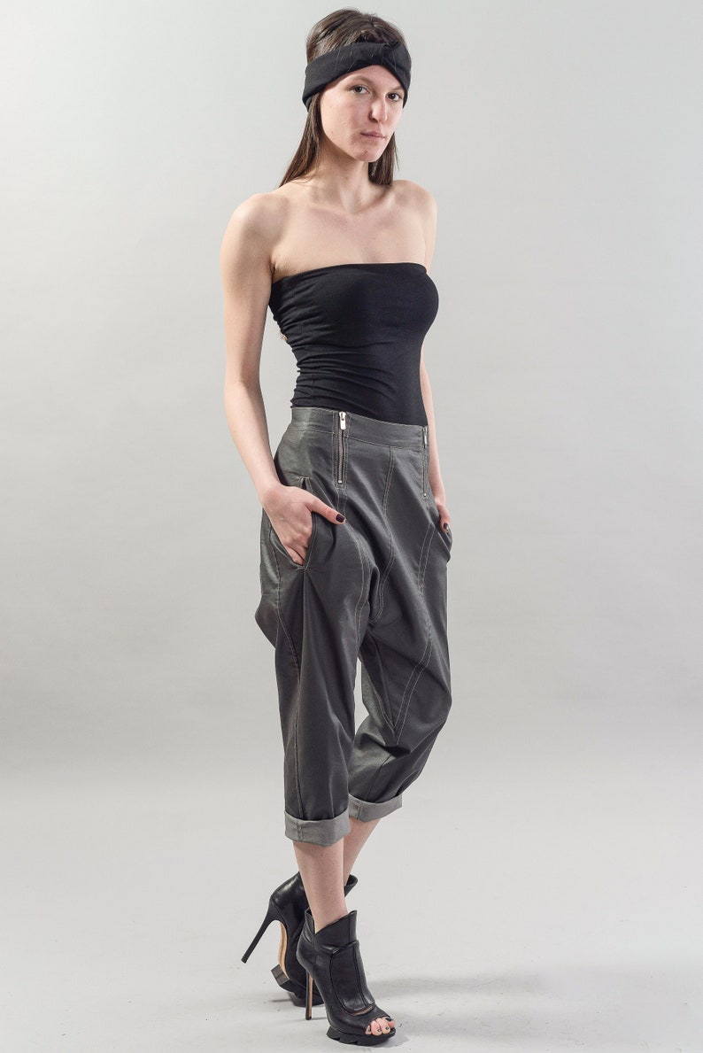 May include: A woman wearing a black strapless top, gray pants with a zipper detail, and black heeled shoes. She is wearing a black headband.