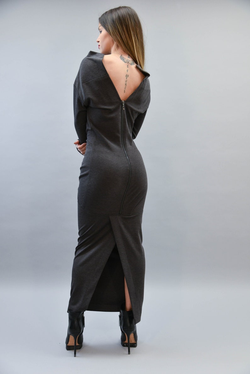 May include: A dark gray, long-sleeved dress with a full-length zipper down the back. The dress has a high neckline that dips low in the back, revealing a portion of the back. The dress is paired with black ankle boots.