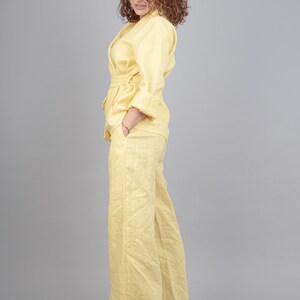 May include: A woman wearing a yellow linen pantsuit with a matching jacket and trousers. The jacket has a wrap style and a belt. The trousers are wide-legged and have a relaxed fit.