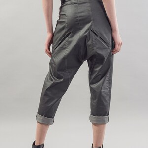May include: Gray cropped pants with a unique design featuring a large pocket on the back. The pants have a cuffed hem and are made of a smooth, slightly shiny fabric.