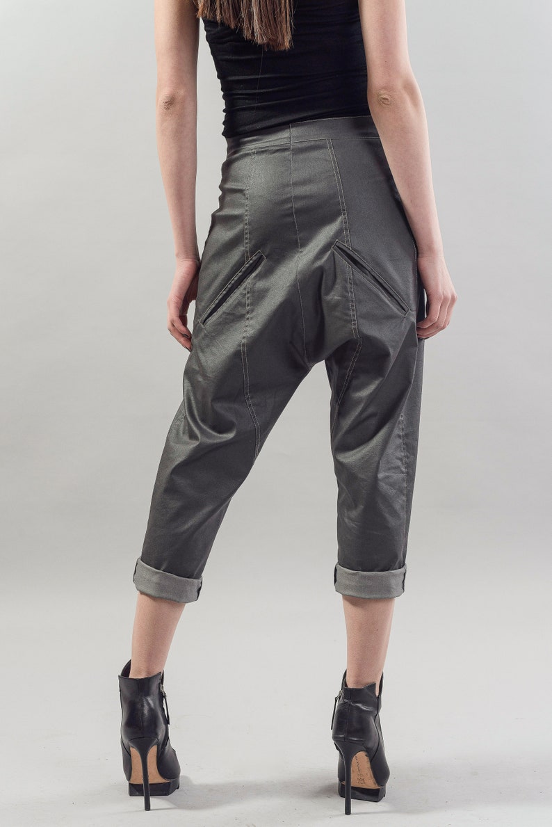 May include: Gray cropped pants with a unique design featuring a large pocket on the back. The pants have a cuffed hem and are made of a smooth, slightly shiny fabric.