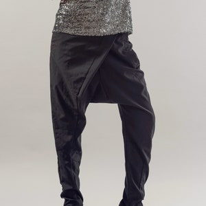 May include: Black trousers with a distinctive draped design and a wide leg silhouette. The trousers are made from a soft, flowing fabric and feature a zip detail at the ankle.