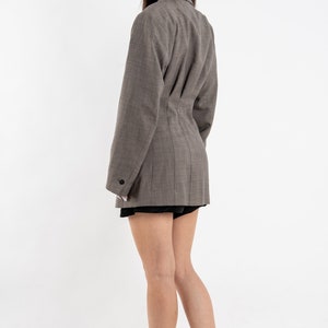 May include: A brown blazer with a fitted waist and long sleeves. The blazer has a single button closure and a notched collar. The model is wearing white sneakers with yellow accents.