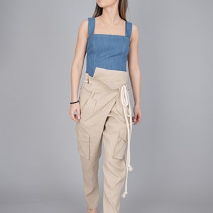 May include: A denim blue square-neck top paired with beige wrap-style cargo pants. The pants feature large pockets and a white rope tie. The outfit is completed with light-colored woven sandals, creating a casual yet stylish ensemble.