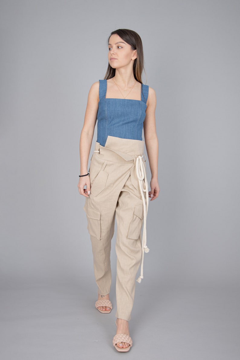 May include: A denim blue square-neck top paired with beige wrap-style cargo pants. The pants feature large pockets and a white rope tie. The outfit is completed with light-colored woven sandals, creating a casual yet stylish ensemble.