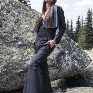 May include: A woman wearing a black leather jacket, black pants, and sunglasses. She is standing in front of a large rock.