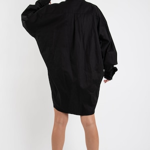 Puede incluir: Un vestido camisa negro de gran tama&ntilde;o con mangas largas y cierre de botones.