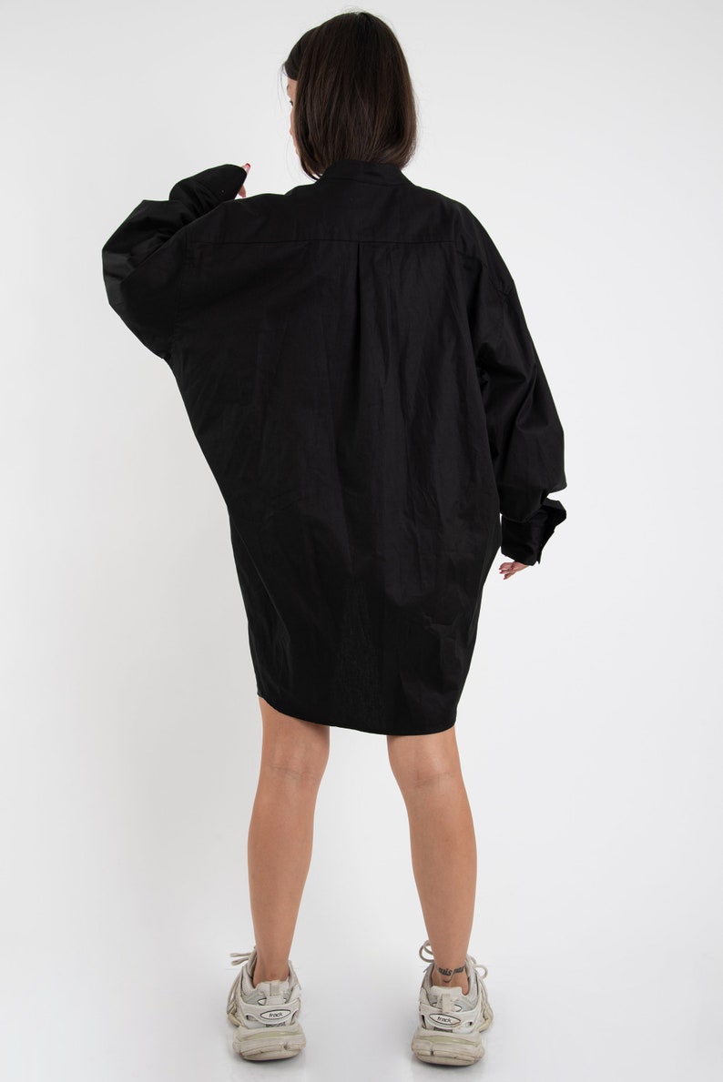 Puede incluir: Un vestido camisa negro de gran tama&ntilde;o con mangas largas y cierre de botones.