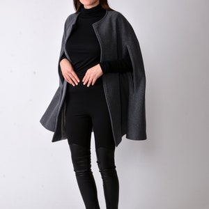 May include: A gray cape with a black turtleneck and black leggings. The person is wearing black leather boots with fur trim.