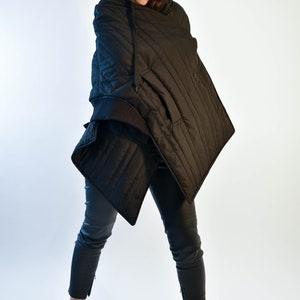 May include: A black quilted hooded jacket with a black baseball cap that says "ICON" on the front. The person is wearing black pants and black and white sneakers.
