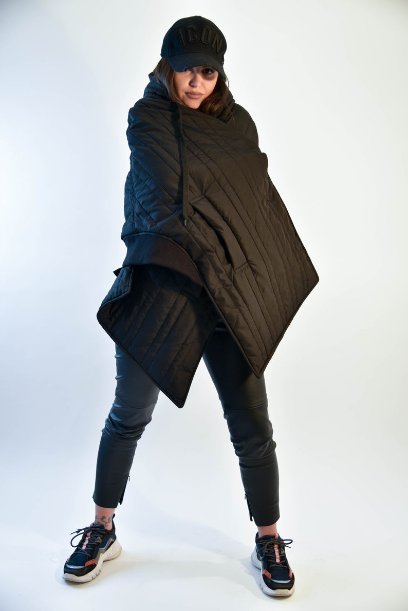 May include: A black quilted hooded jacket with a black baseball cap that says "ICON" on the front. The person is wearing black pants and black and white sneakers.