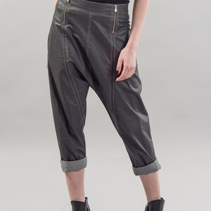 May include: Gray leather pants with a cuffed hem and zipper detailing. The pants have a loose fit and are styled with black heeled ankle boots.