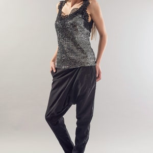 May include: A woman wearing a black sequined tank top with a lace trim and black trousers. She is wearing black sunglasses and has long brown hair.