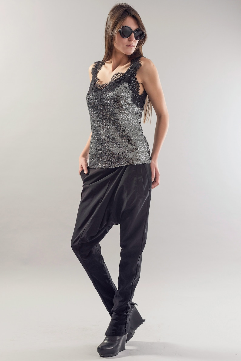May include: A woman wearing a black sequined tank top with a lace trim and black trousers. She is wearing black sunglasses and has long brown hair.