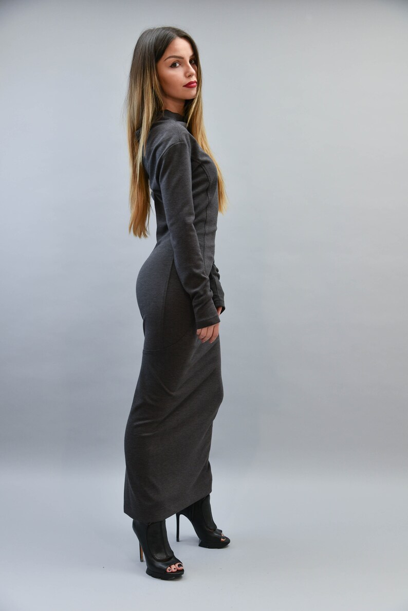 May include: A long, dark gray dress with long sleeves and a high neckline. The dress is form-fitting and reaches the floor. The person is wearing black open-toe high heels. The background is a solid light gray.