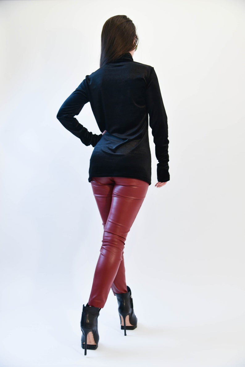 May include: A woman wearing a black turtleneck sweater and red leather pants. She is wearing black heeled boots.