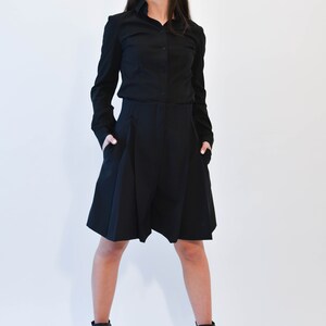 May include: A woman wearing a black long-sleeved shirt and black shorts with a pleated design. She is wearing black heeled ankle boots.
