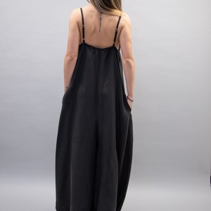 May include: A black sleeveless jumpsuit with a loose, flowing fit. The jumpsuit has a scoop neck and a gathered waist.