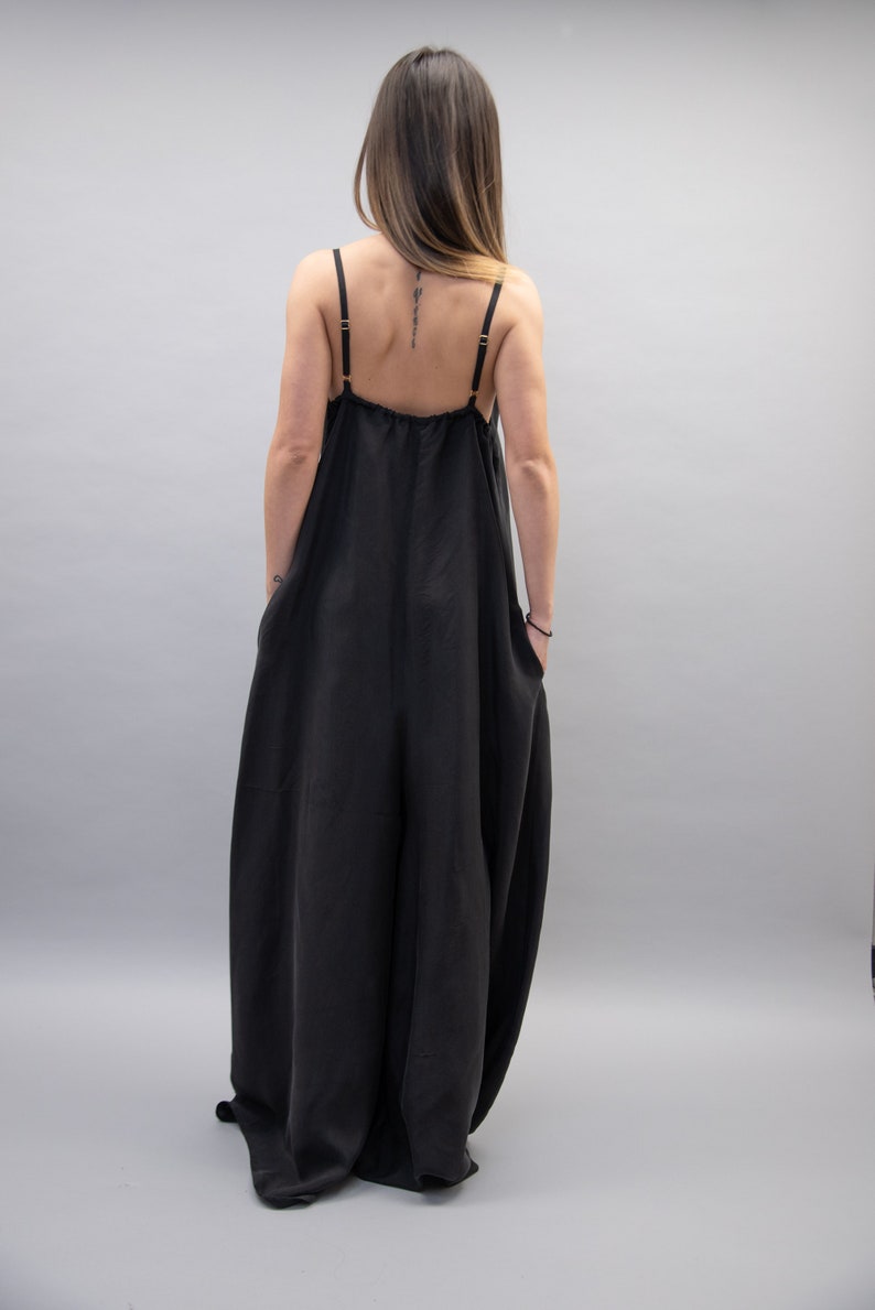 May include: A black sleeveless jumpsuit with a loose, flowing fit. The jumpsuit has a scoop neck and a gathered waist.