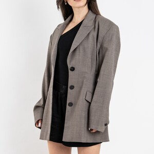 May include: A gray blazer with a black button closure and a black top underneath. The blazer has a long, relaxed fit and is made of a textured fabric.