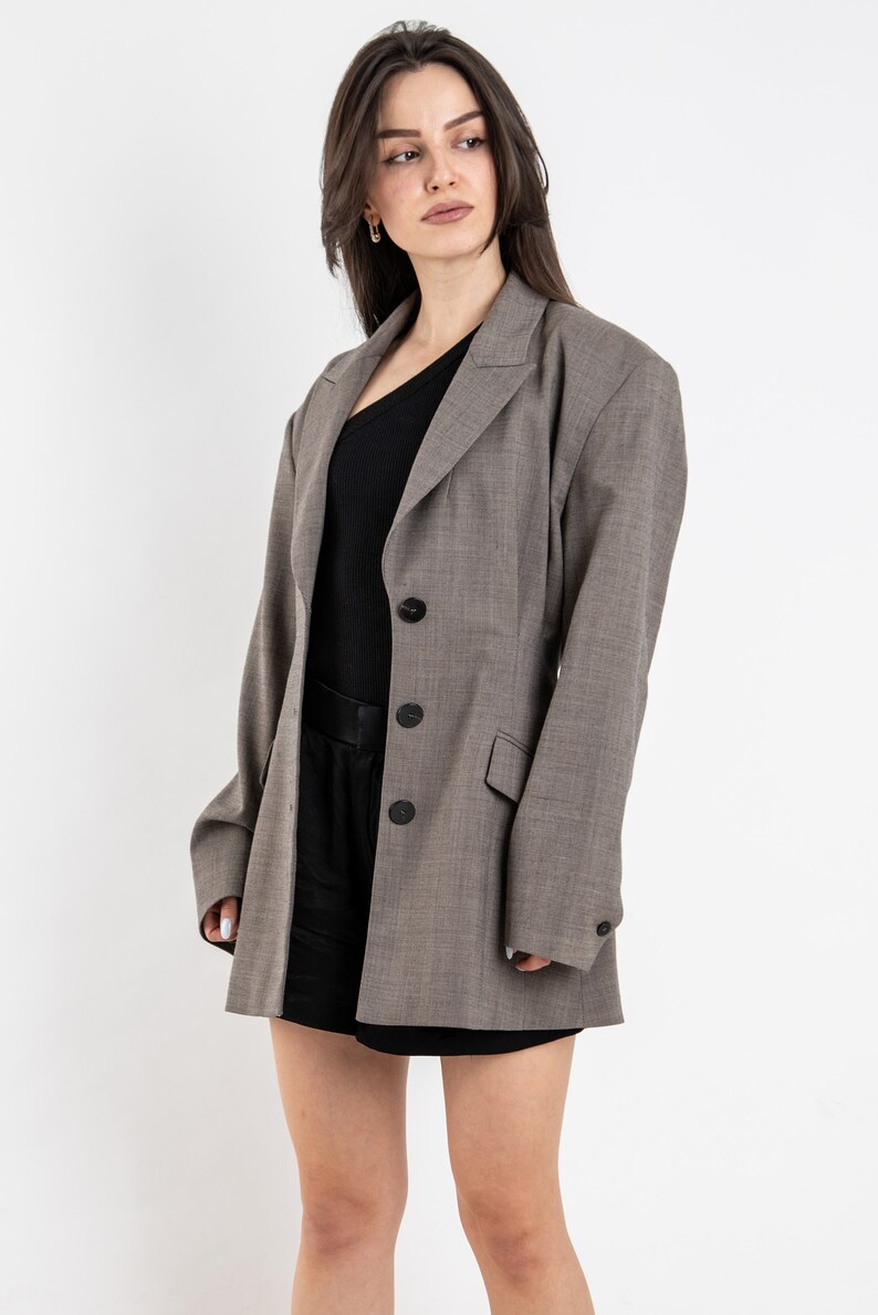 May include: A gray blazer with a black button closure and a black top underneath. The blazer has a long, relaxed fit and is made of a textured fabric.