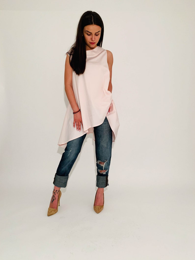 May include: A woman is wearing a pink sleeveless top with a high-low hemline and blue jeans with rolled cuffs. She is wearing brown suede heels.