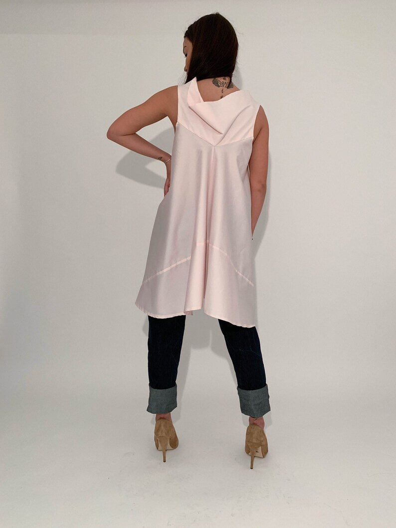 May include: A pink sleeveless tunic top with a cowl neck and a high-low hemline. The tunic is worn with dark blue jeans that have been rolled up at the ankles.