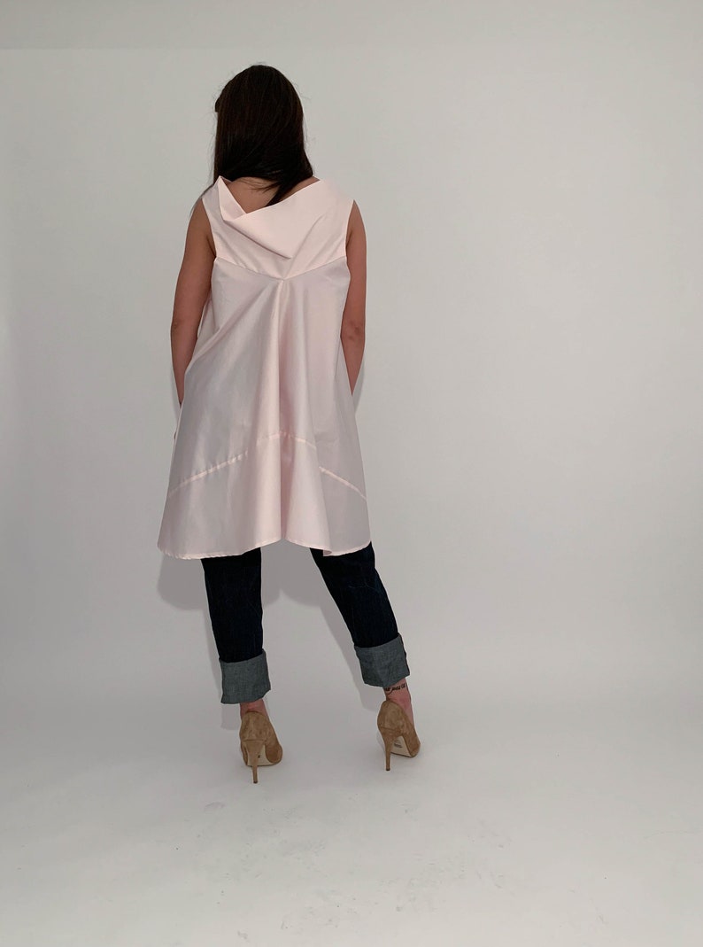 May include: A pink sleeveless tunic top with a cowl neck and a flowing, asymmetrical hemline. The top is worn with dark blue jeans and brown heeled shoes.
