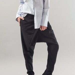 May include: A woman wearing a light blue striped button-down shirt and black trousers with a unique design. The trousers have a wide leg and a gathered detail at the ankle.
