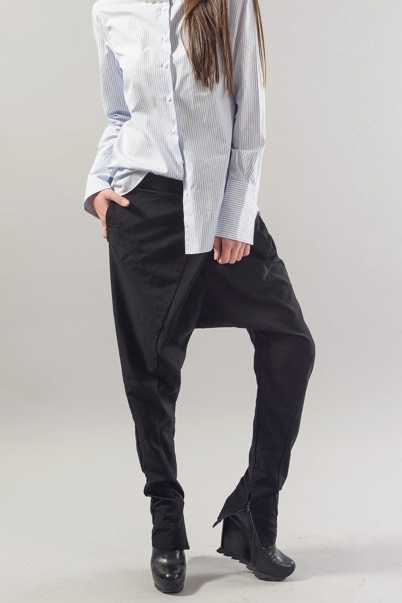 May include: A woman wearing a light blue striped button-down shirt and black trousers with a unique design. The trousers have a wide leg and a gathered detail at the ankle.
