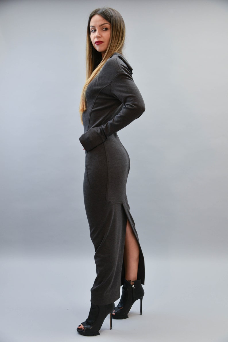 May include: A dark gray, long-sleeved dress with a high slit on the side. The dress is paired with black high-heeled ankle boots. The model is standing in front of a gray background.
