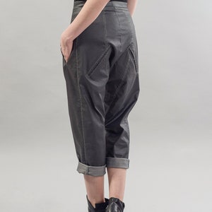 May include: A pair of dark gray cropped pants with a unique design and cuffed hems. The pants are made of a smooth, slightly shiny fabric and have a relaxed fit.