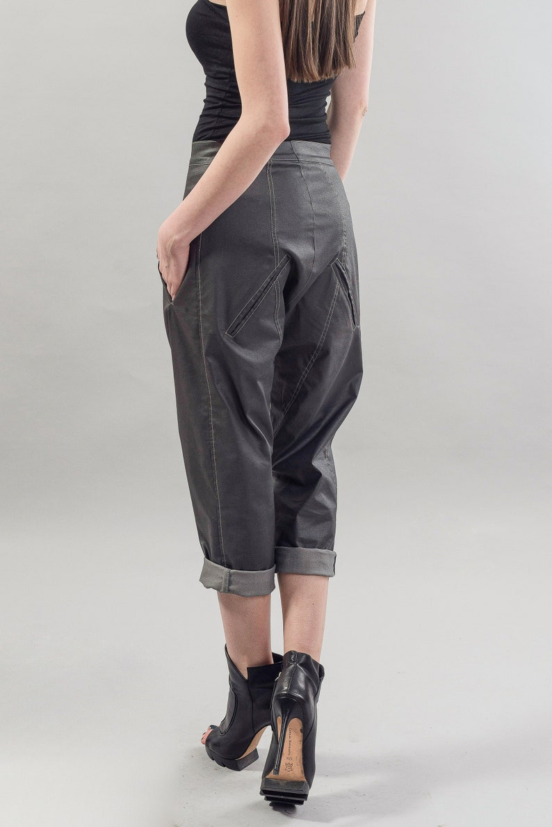 May include: A pair of dark gray cropped pants with a unique design and cuffed hems. The pants are made of a smooth, slightly shiny fabric and have a relaxed fit.