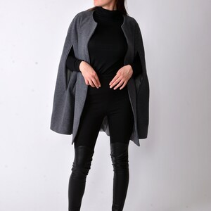 May include: A woman wearing a gray cape with black leggings and black fur-trimmed loafers. She is wearing sunglasses and has red lipstick.