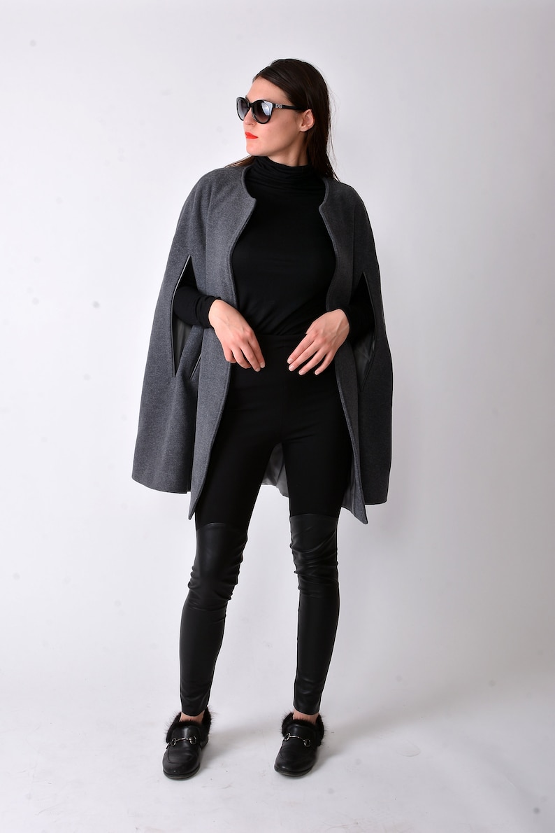 May include: A woman wearing a gray cape with black leggings and black fur-trimmed loafers. She is wearing sunglasses and has red lipstick.