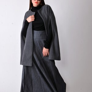 May include: A woman wearing a gray cape and a long gray skirt with a black turtleneck shirt and black sunglasses.