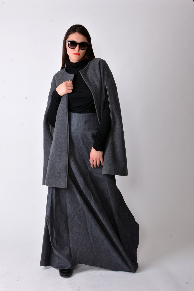 May include: A woman wearing a gray cape and a long gray skirt with a black turtleneck shirt and black sunglasses.