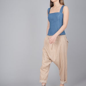 May include: A woman wearing a blue denim sleeveless top and beige, loose-fitting trousers. She is wearing light brown heeled sandals.